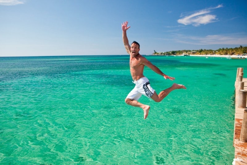 man jumping into turquoise water in Honduras