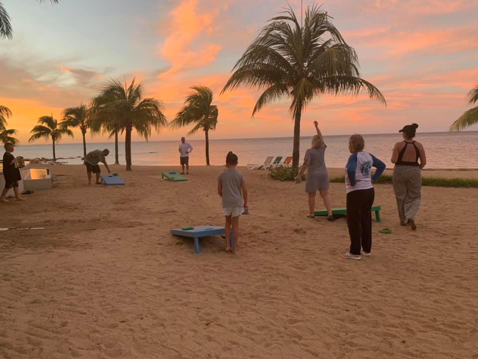 a multi-generational vacation with everyone playing cornhole on the beach as the sun sets